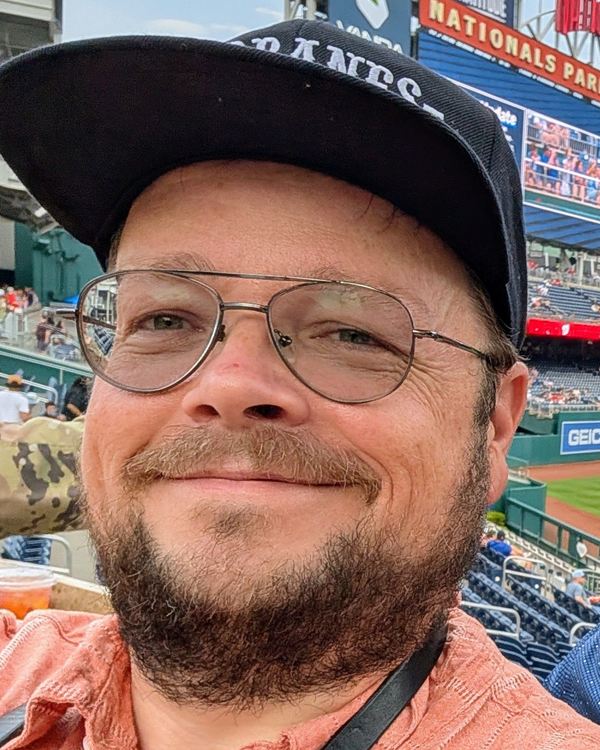Cary Stolarczyk, smiling, wearing glasses and a ball cap